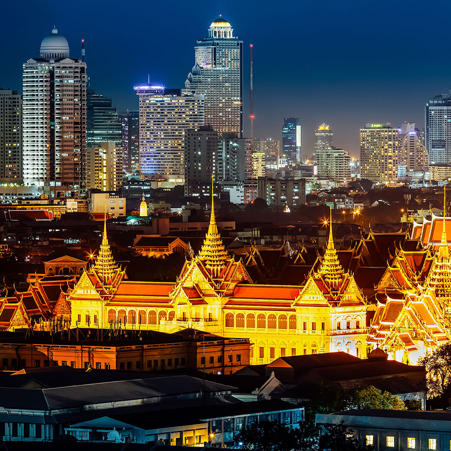 Gran Palacio de Bangkok  iluminado en la noche, con el horizonte de la ciudad al fondo. Descubre Tailandia con Viajes Comfama